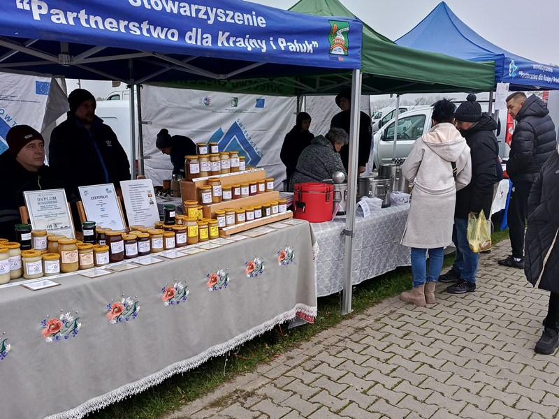 Stoisko LGD: pod namiotem stoi stół, a na nim miody. Za stołem stoją dwaj wytwórcy lokalni.