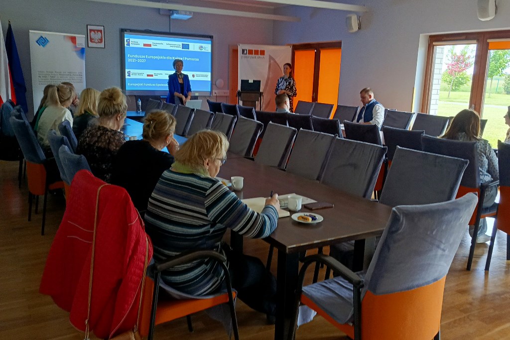 Uczestnicy szkolenia na pierwszym planie - siedzą przy stołach i słuchają prowadzących. W tle dyrektor biura LGD.